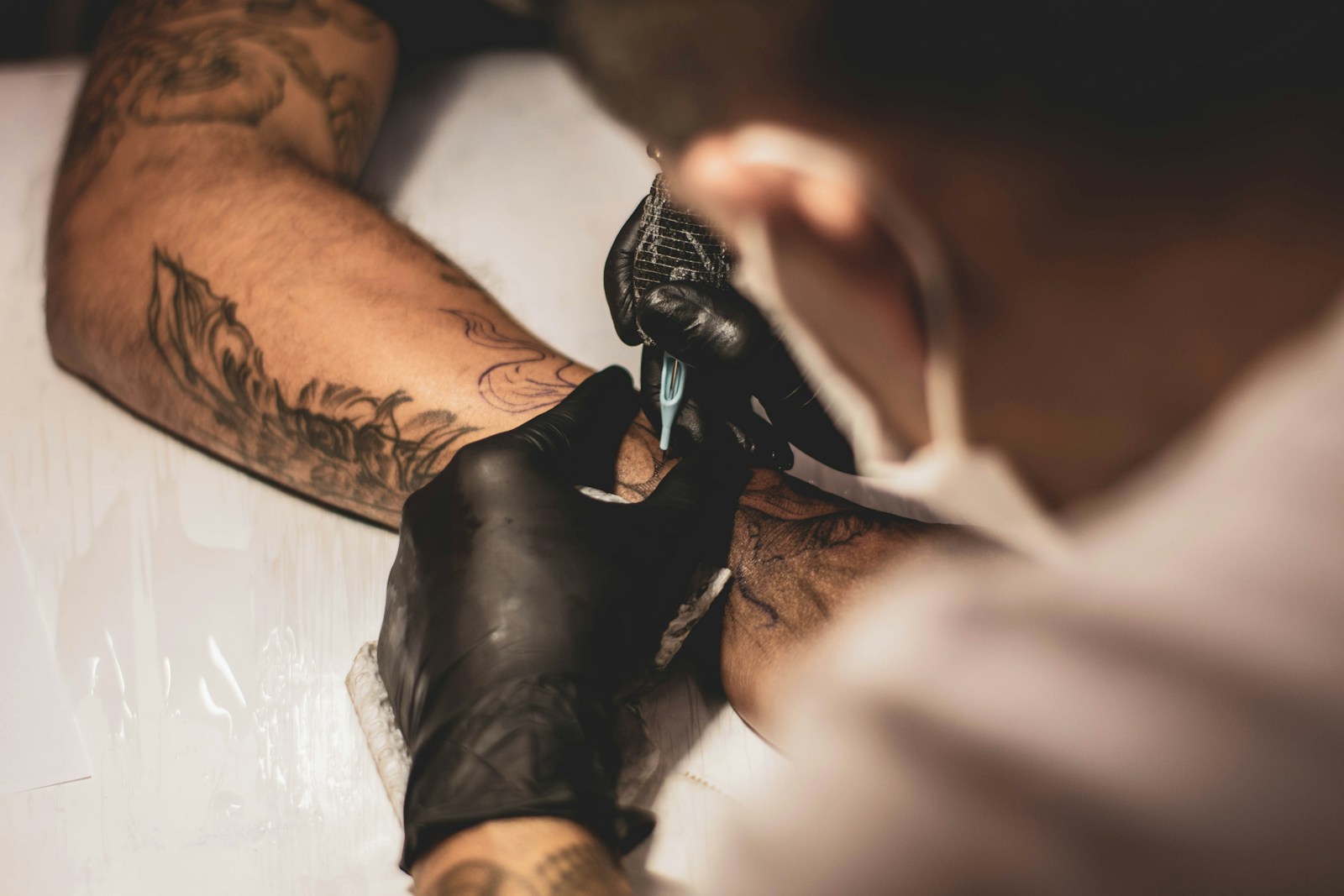 Detalhe do processo de tatuagem, com mãos enluvadas e máquina de tatuar